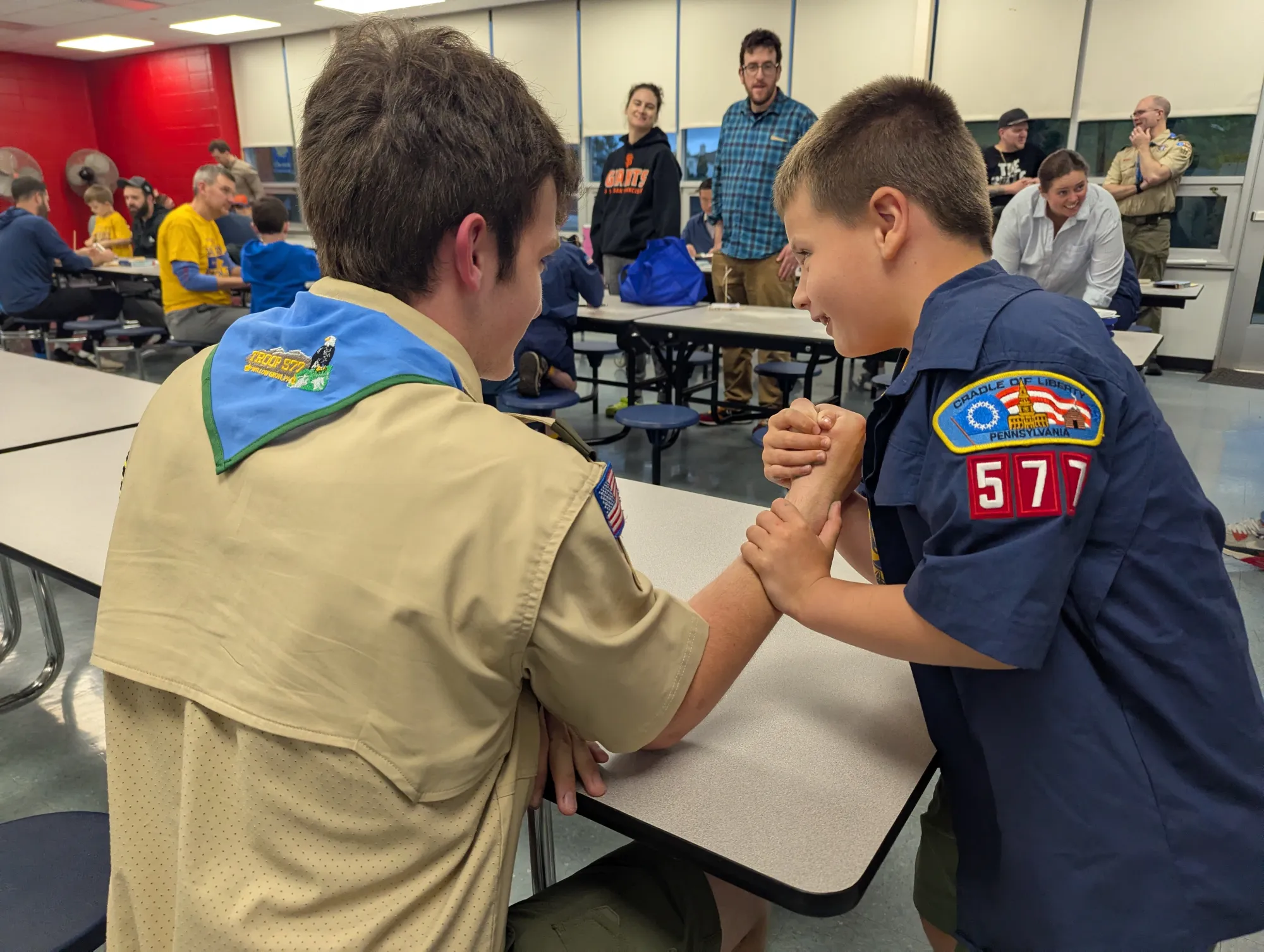 A Cub Scout arm wrestles an older Scout